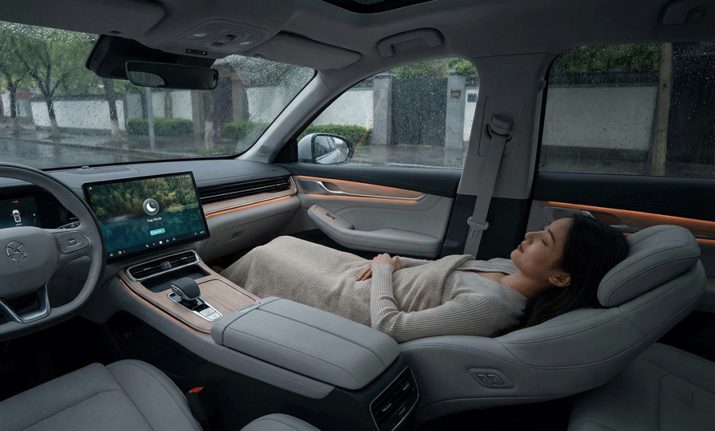 The interior of a Chinese electric car configured for sleep, with the passenger seat reclined flat and a person resting, while it rains outside.