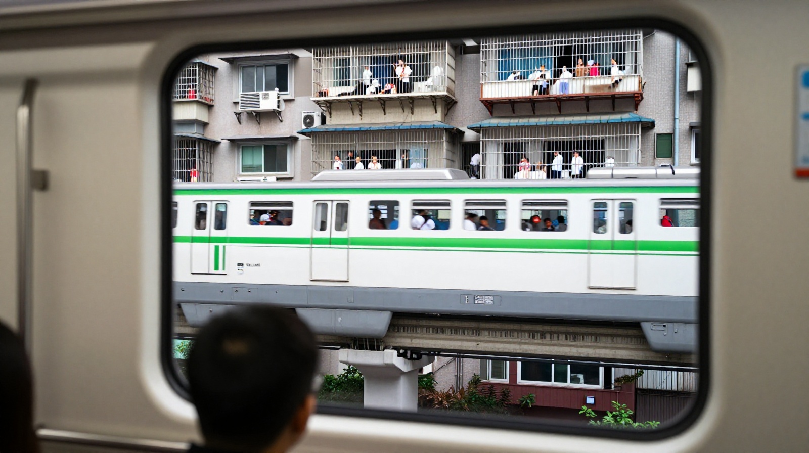 Passengers inside Chongqing's light rail looking out the window as the train passes through a residential apartment building with balconies visible.