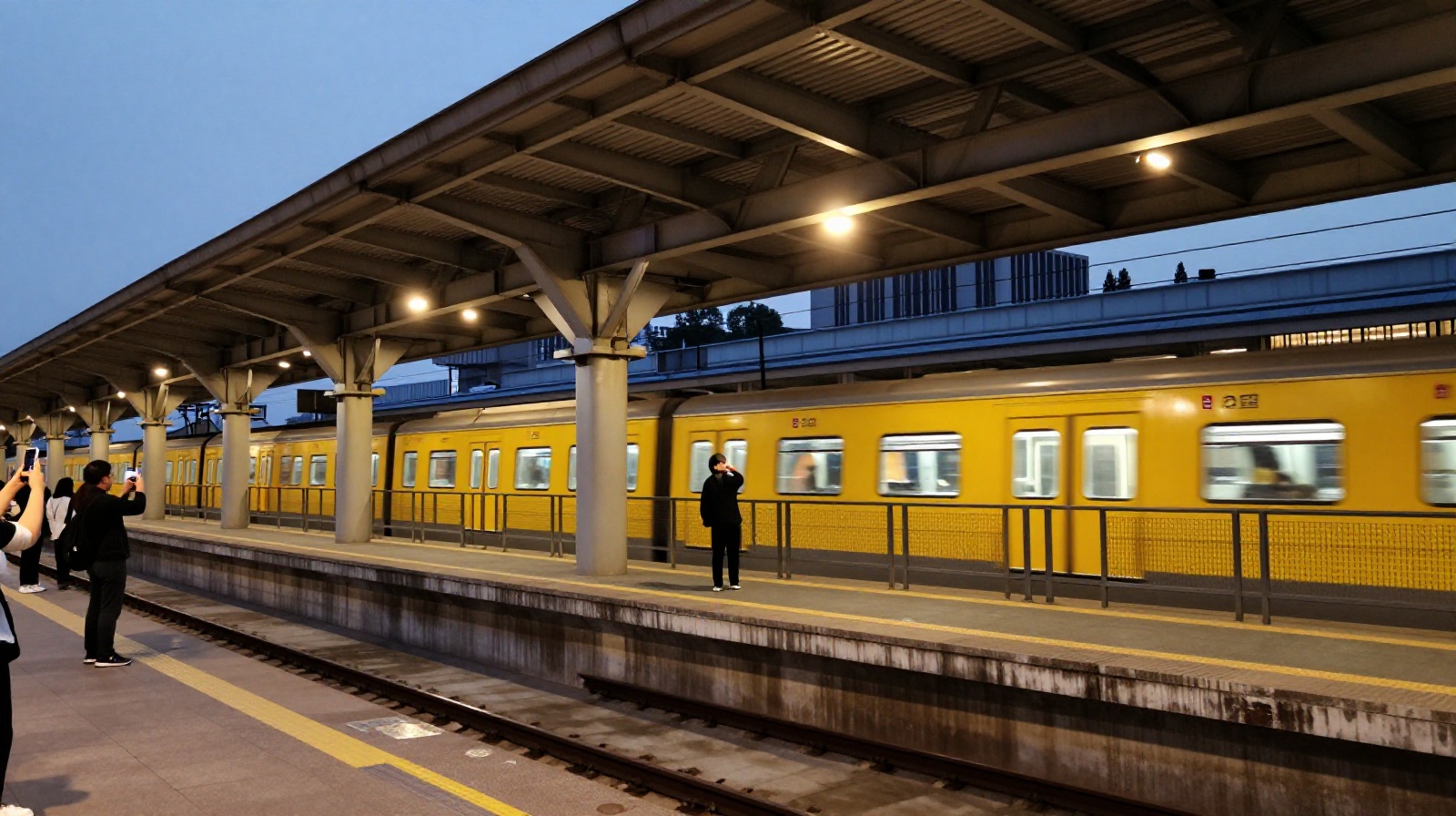 Tourists and locals taking photos on the Liziba Station platform as a light rail train passes through a building in Chongqing at dusk.