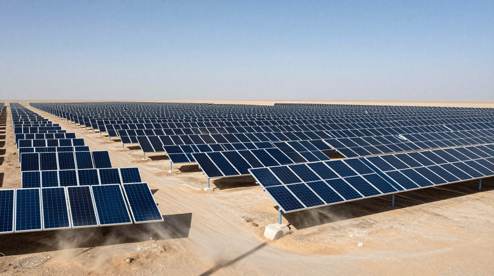 Rows of solar panels covering a vast area of desert land under a clear blue sky