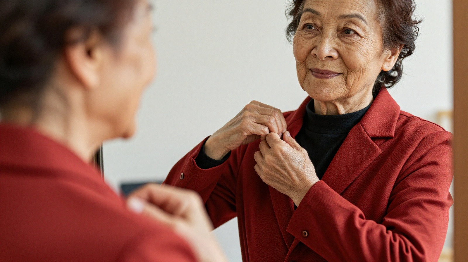 70-year-old Chinese woman Li Hua adjusting her vibrant red blazer and yellow sneakers while looking in a mirror at home