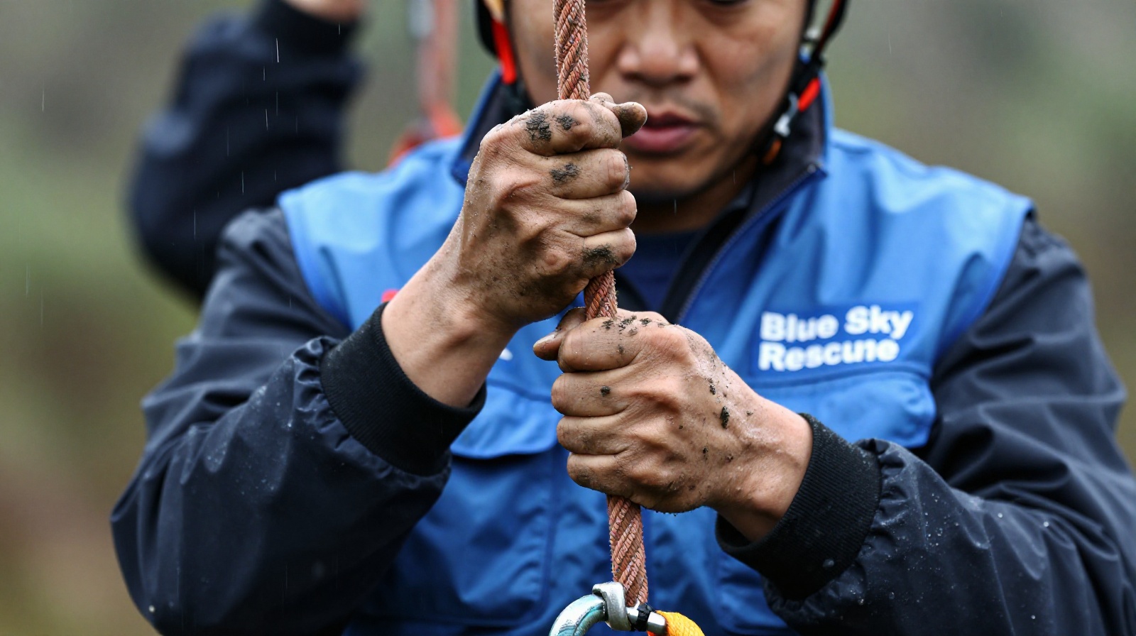 Close up of muddy hands holding rescue rope worn by blue sky rescue volunteer
