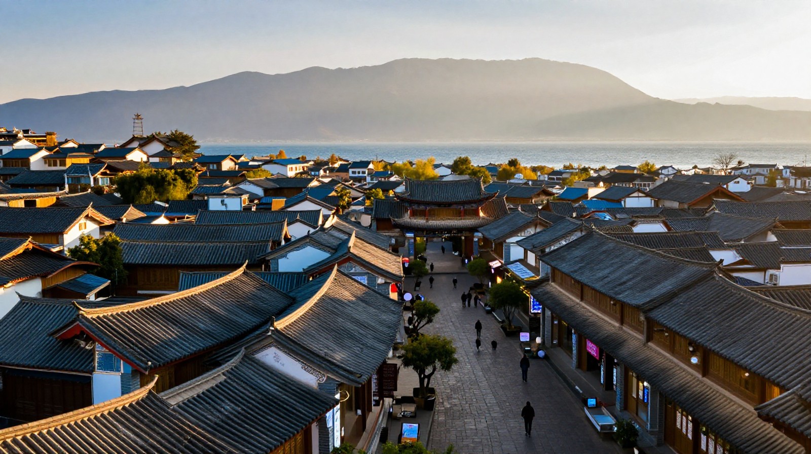 Scenic aerial landscape of Dali Ancient Town featuring traditional buildings, a lake, and mountains under a golden sunset sky