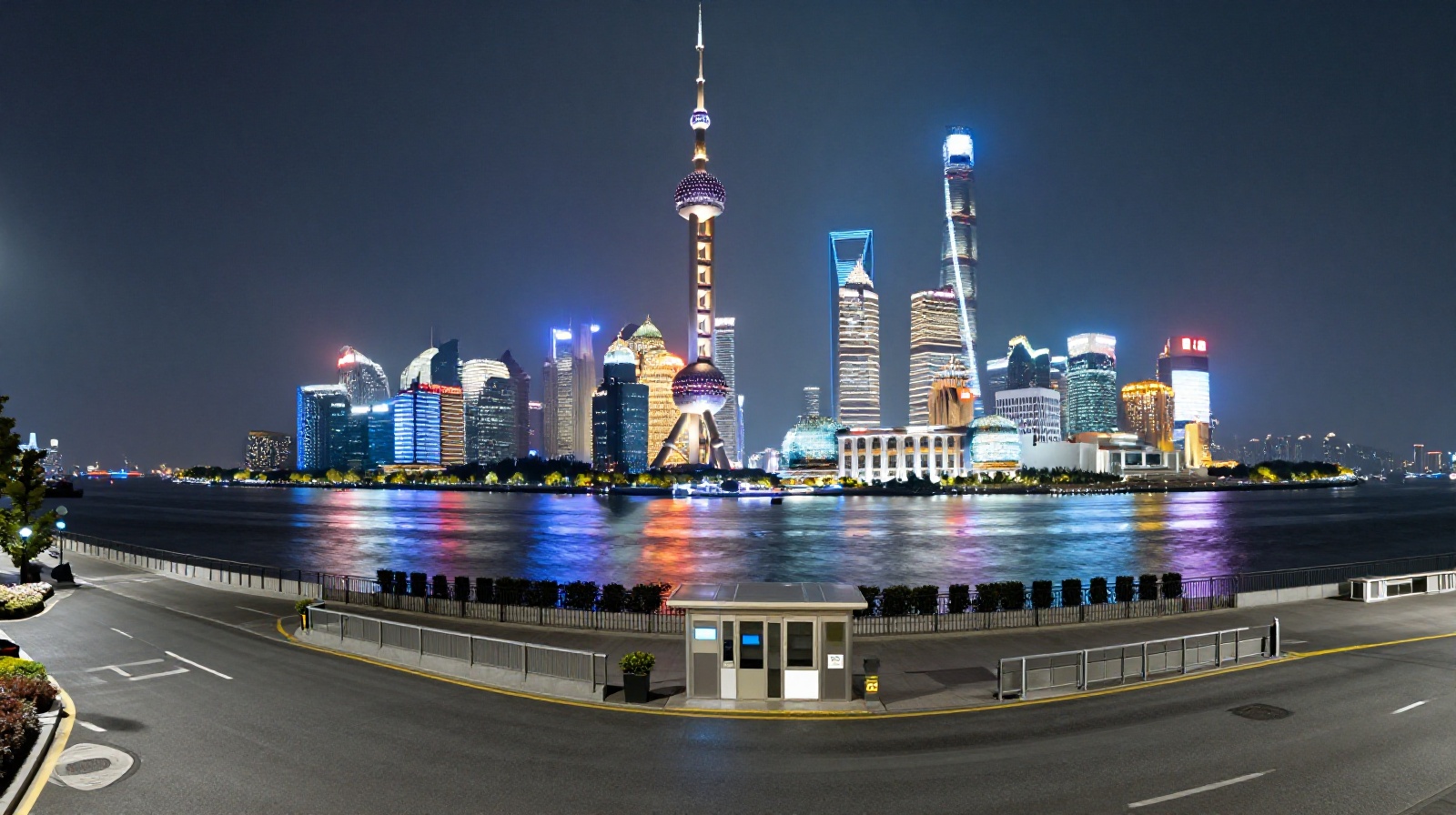 The quiet Shanghai Bund at night with towering skyscrapers reflected in the river and a modern security booth monitoring the area