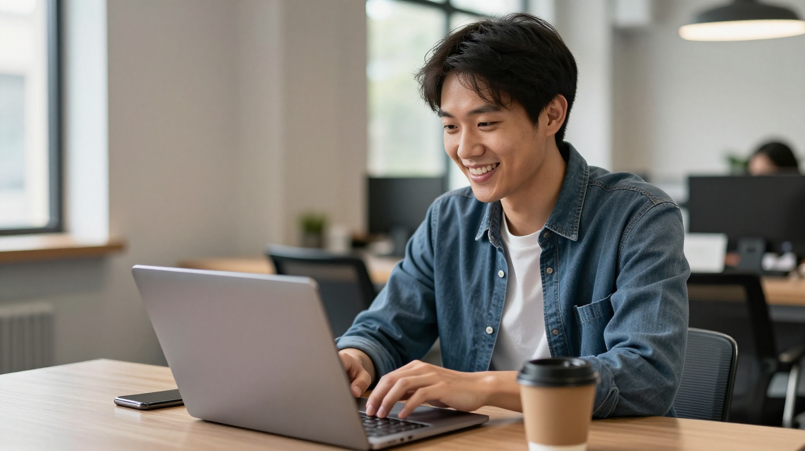 A happy young entrepreneur reviewing business documents on a laptop in a modern co-working space.