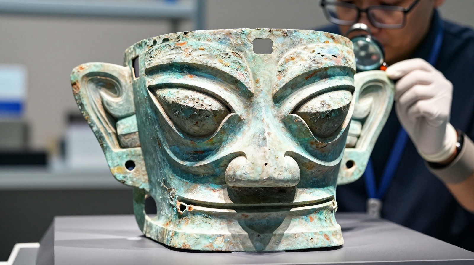 Close-up view of a Sanxingdui bronze mask with protruding eyes displayed in a laboratory setting with an archaeologist working nearby