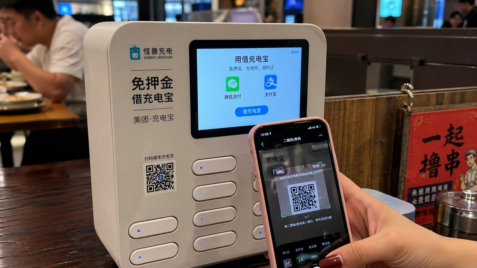 Close-up of a user scanning a QR code to rent a shared power bank at a Chinese restaurant table