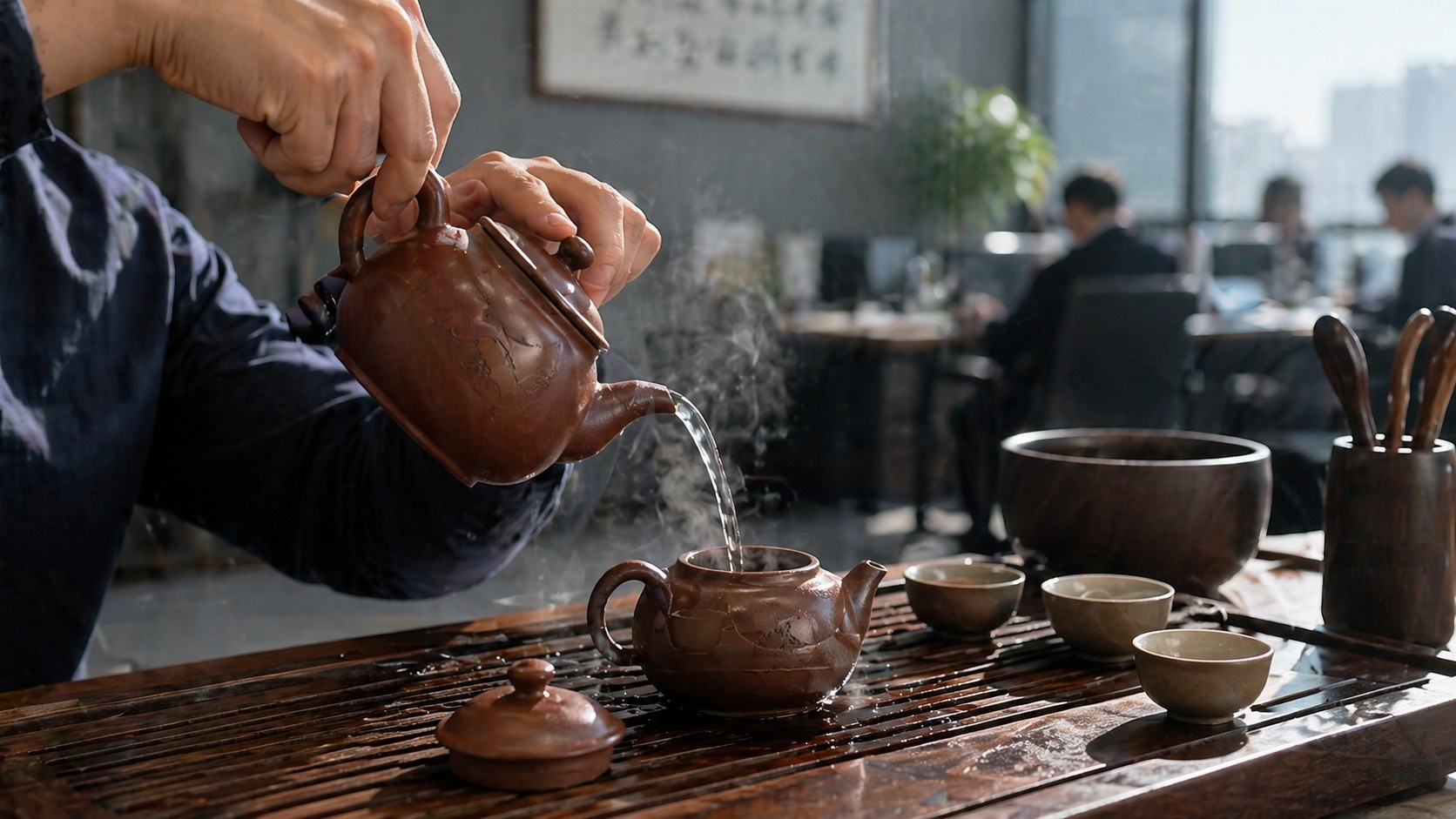 Close-up of hands performing Chaoshan Gongfu tea pouring technique with steam rising from a clay teapot in an office setting