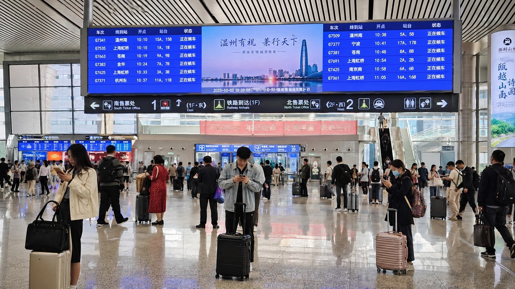 Passengers at a modern Chinese high-speed rail station checking real-time schedules on digital displays and mobile phones.