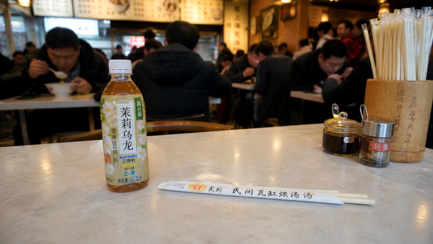 A water bottle and chopsticks placed on a table to save a seat at a busy Chinese breakfast shop.