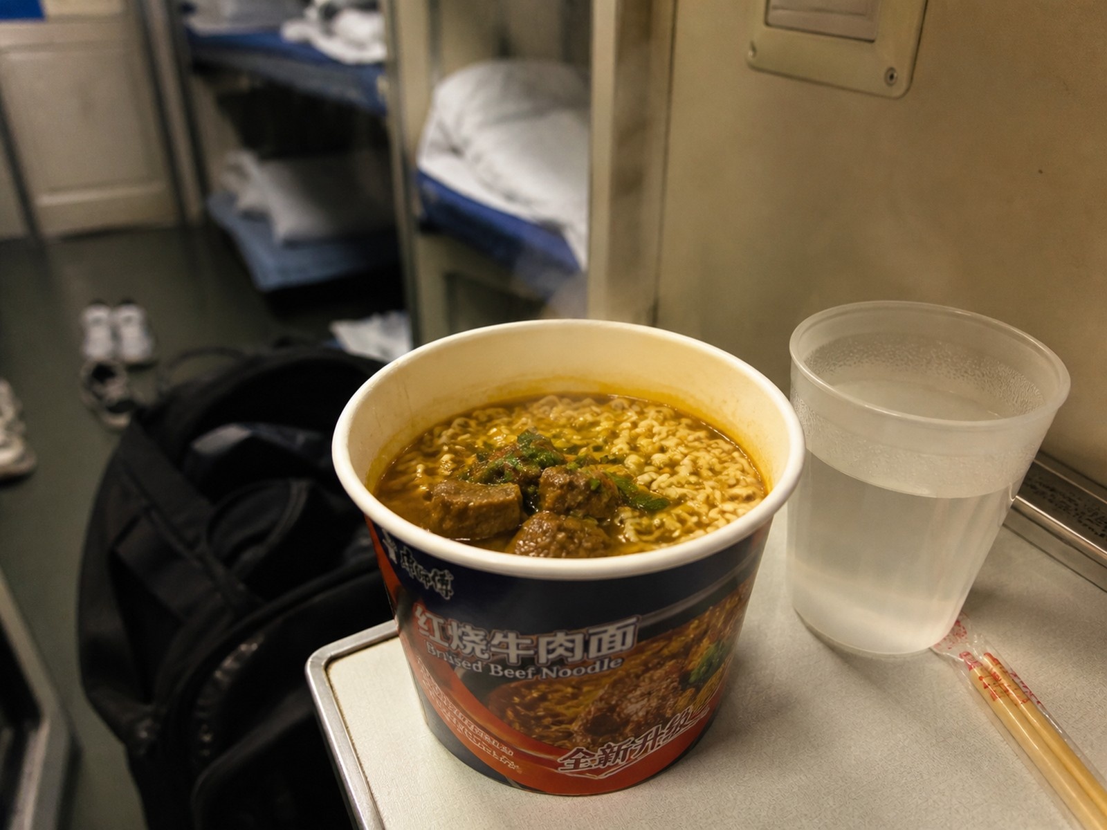 Steaming bowl of instant noodles and hot water on a sleeper train table, a staple of Chinese rail travel.