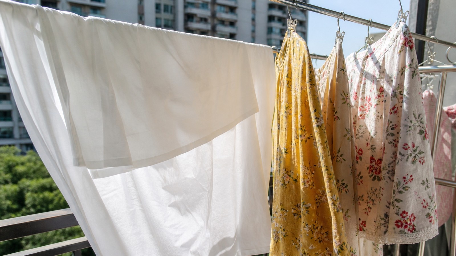 Sunlight hitting white linen and colorful shirts drying on an outdoor balcony rack in a Chinese apartment.
