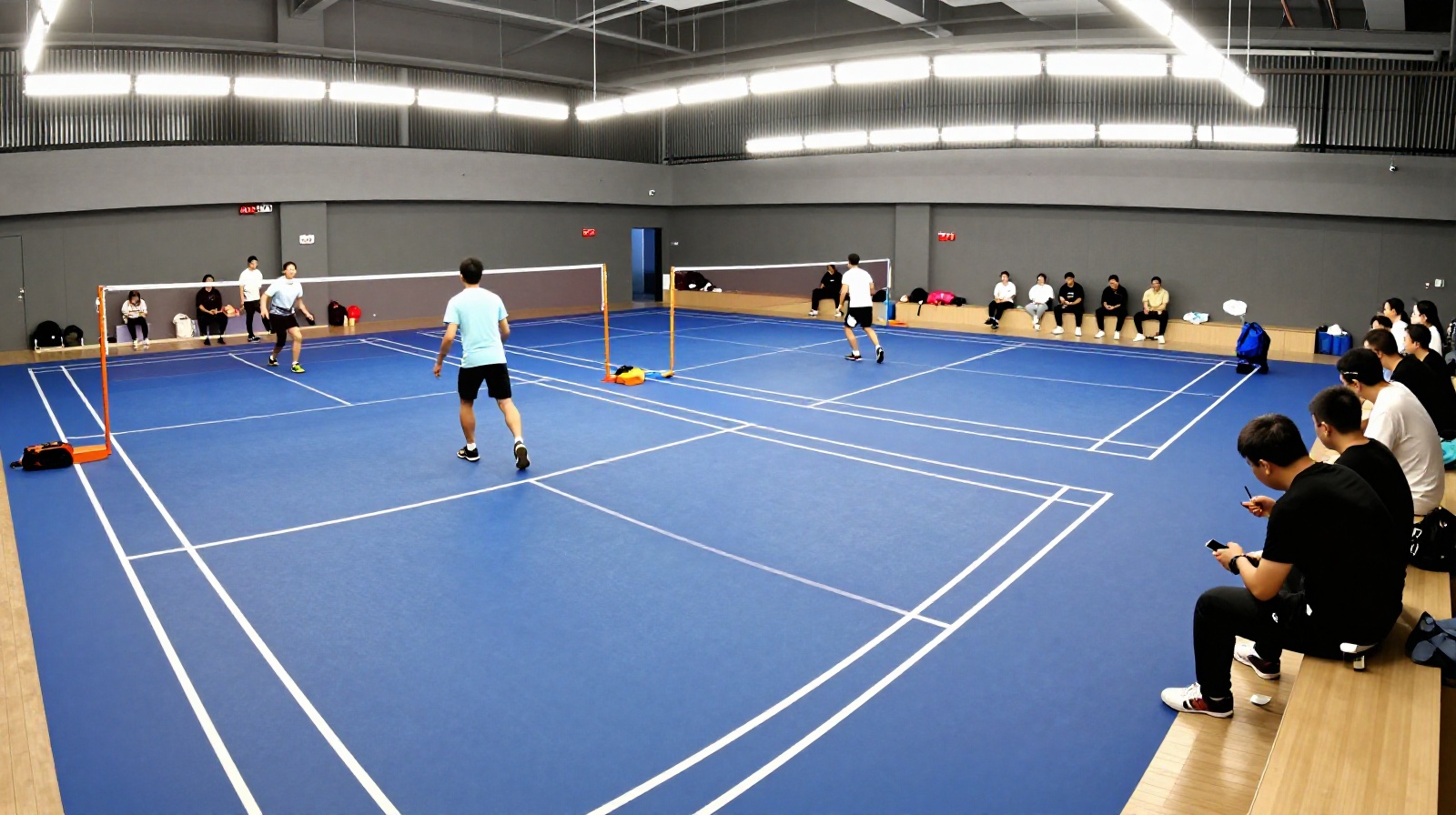 An indoor badminton court in a Chinese city with multiple groups of people playing casual games during an evening session.