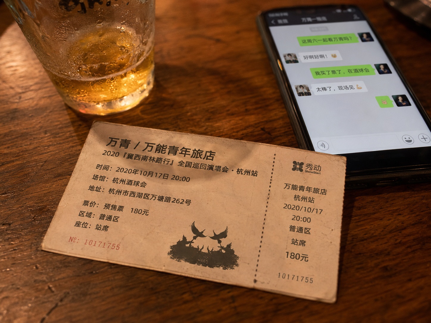 A concert ticket stub for an independent band in China placed on a bar counter next to a drink and a phone, symbolizing entry into the live music scene.