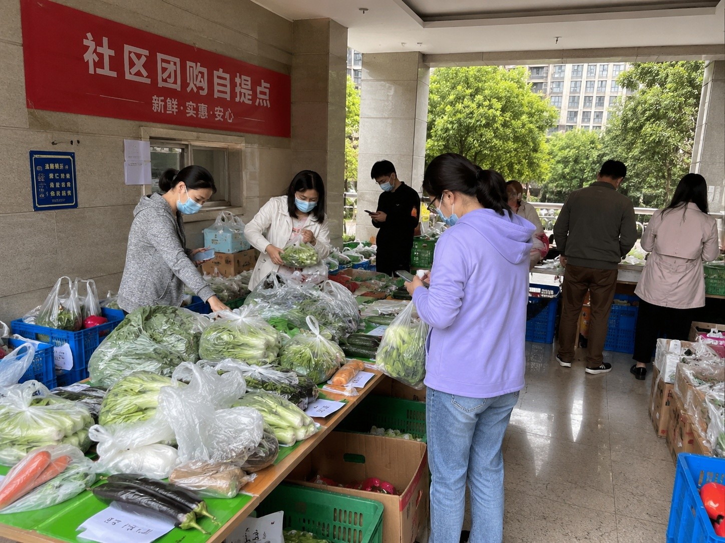 Residents picking up fresh vegetables from a community group buying pickup point in a Chinese residential building lobby.