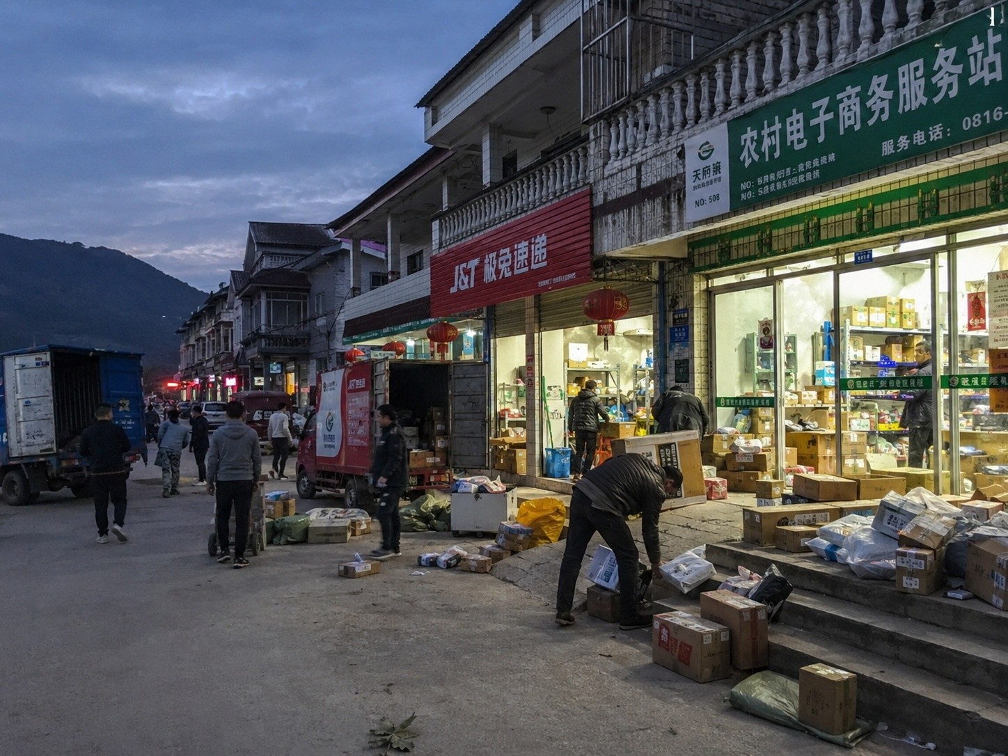 Busy street in a Chinese jade village with delivery trucks and active storefronts, illustrating the logistics network.