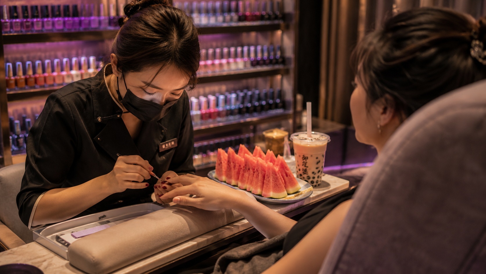 A nail technician applying gel polish to a client in a modern Chinese nail salon, showing the service interaction.