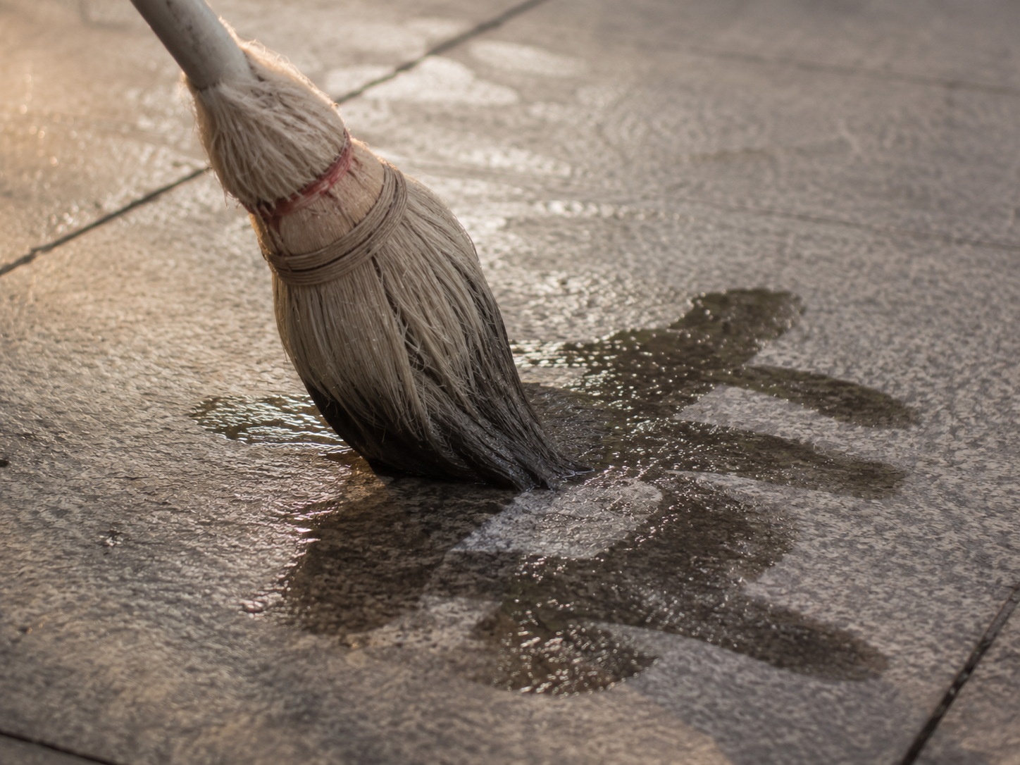 Close-up of a giant water sponge brush writing Chinese characters on wet pavement in a park