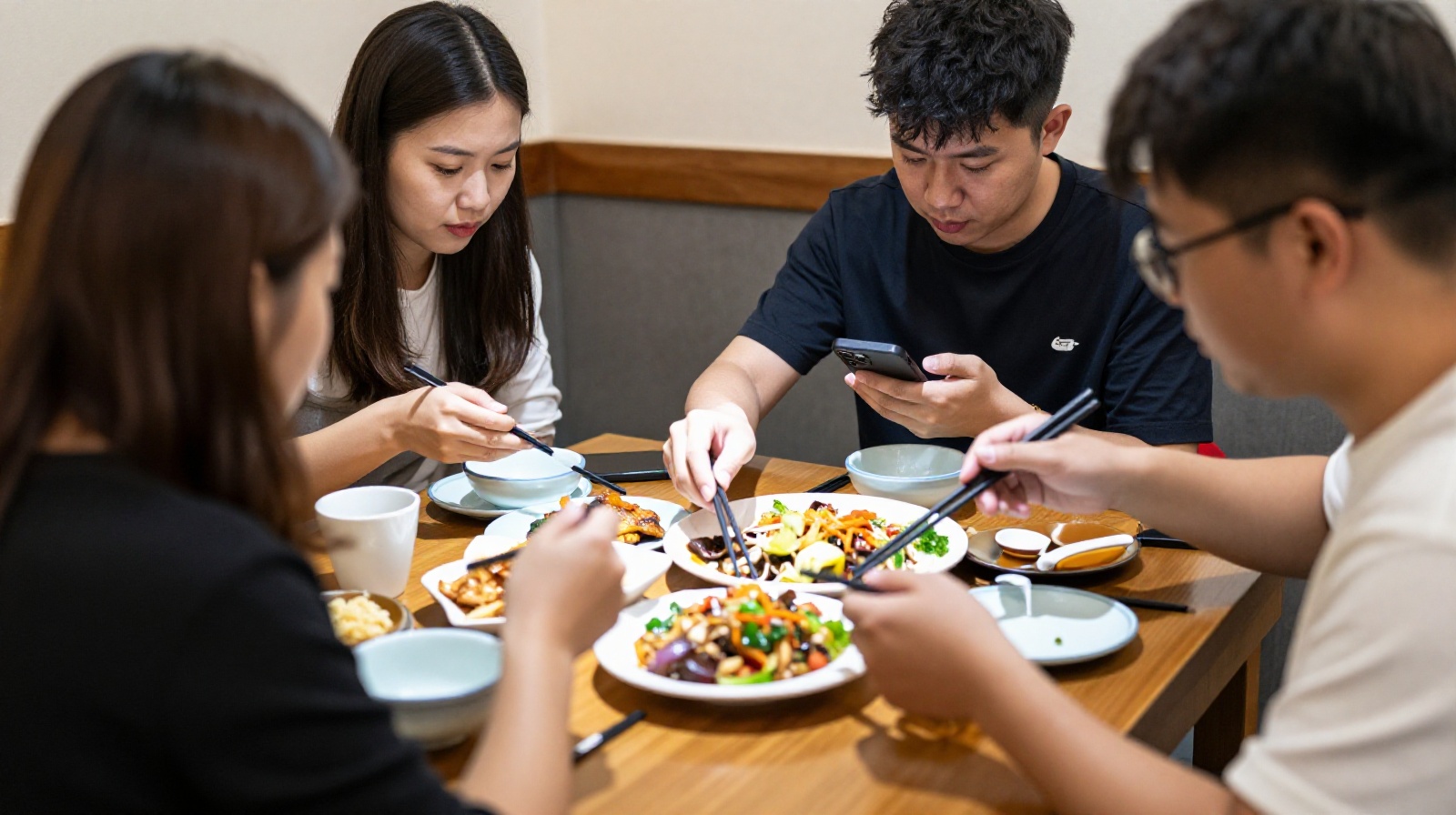 Four strangers sharing a small table in a busy Chinese restaurant, demonstrating polite distance while dining together.