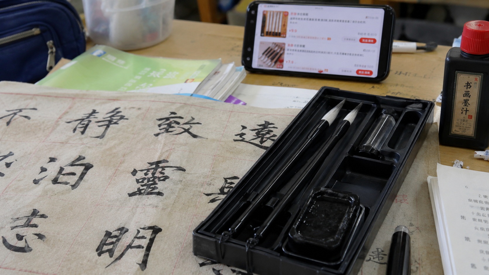 A budget-friendly calligraphy set for students on a modern desk, showing synthetic brushes and simple paper, reflecting the low-cost entry level of Chinese traditional art supplies.
