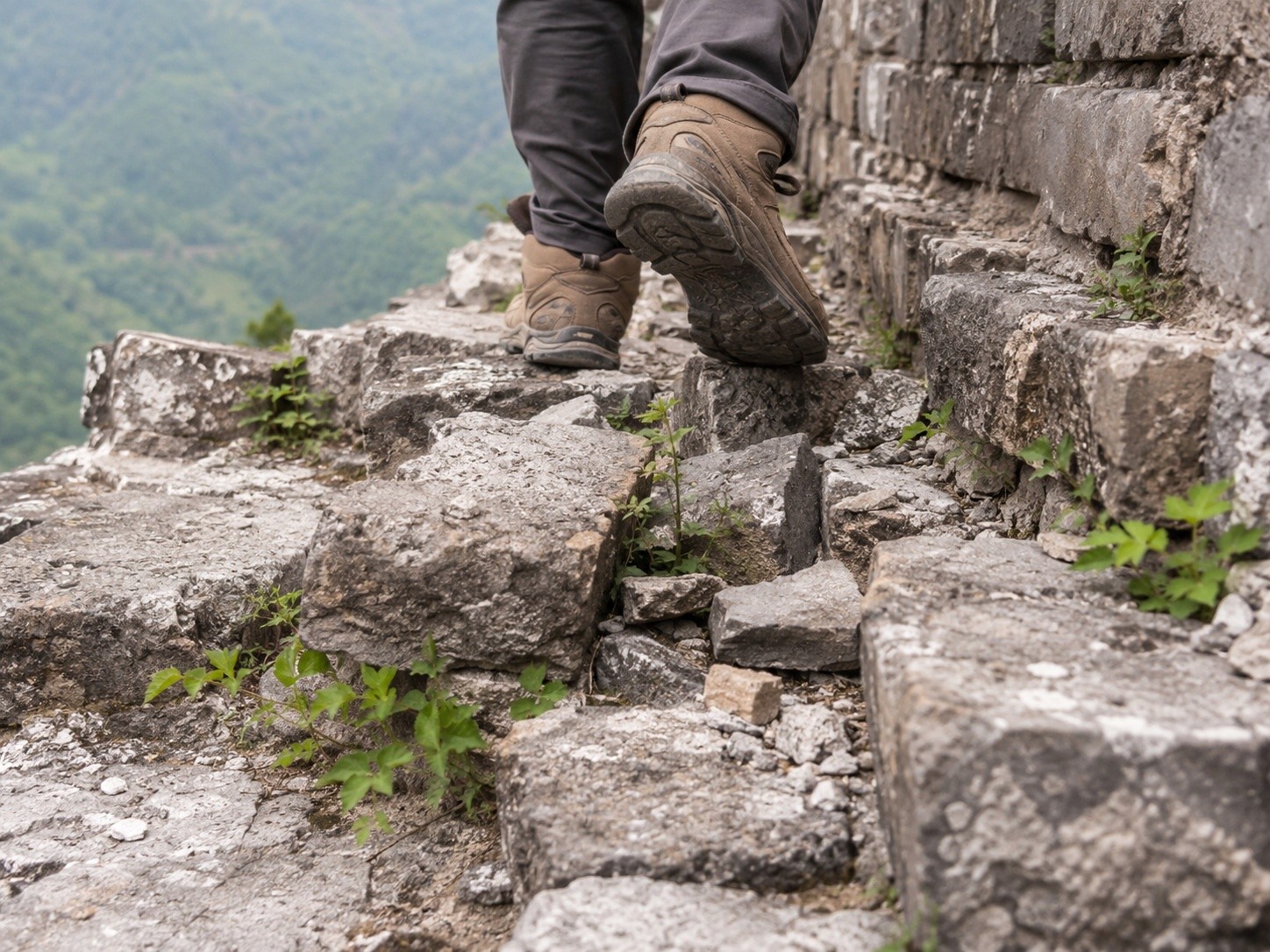 A hiker's boots stepping carefully on the loose and uneven stones of the Wild Great Wall, showing the difficult terrain.