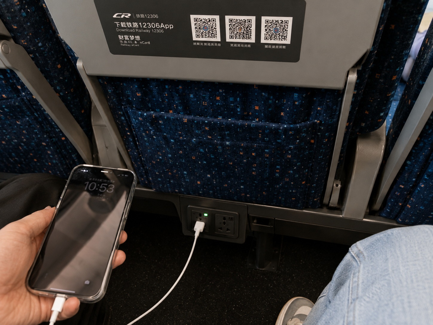 Close-up of power outlet under the seat in second class Chinese high-speed train, phone cable plugged in