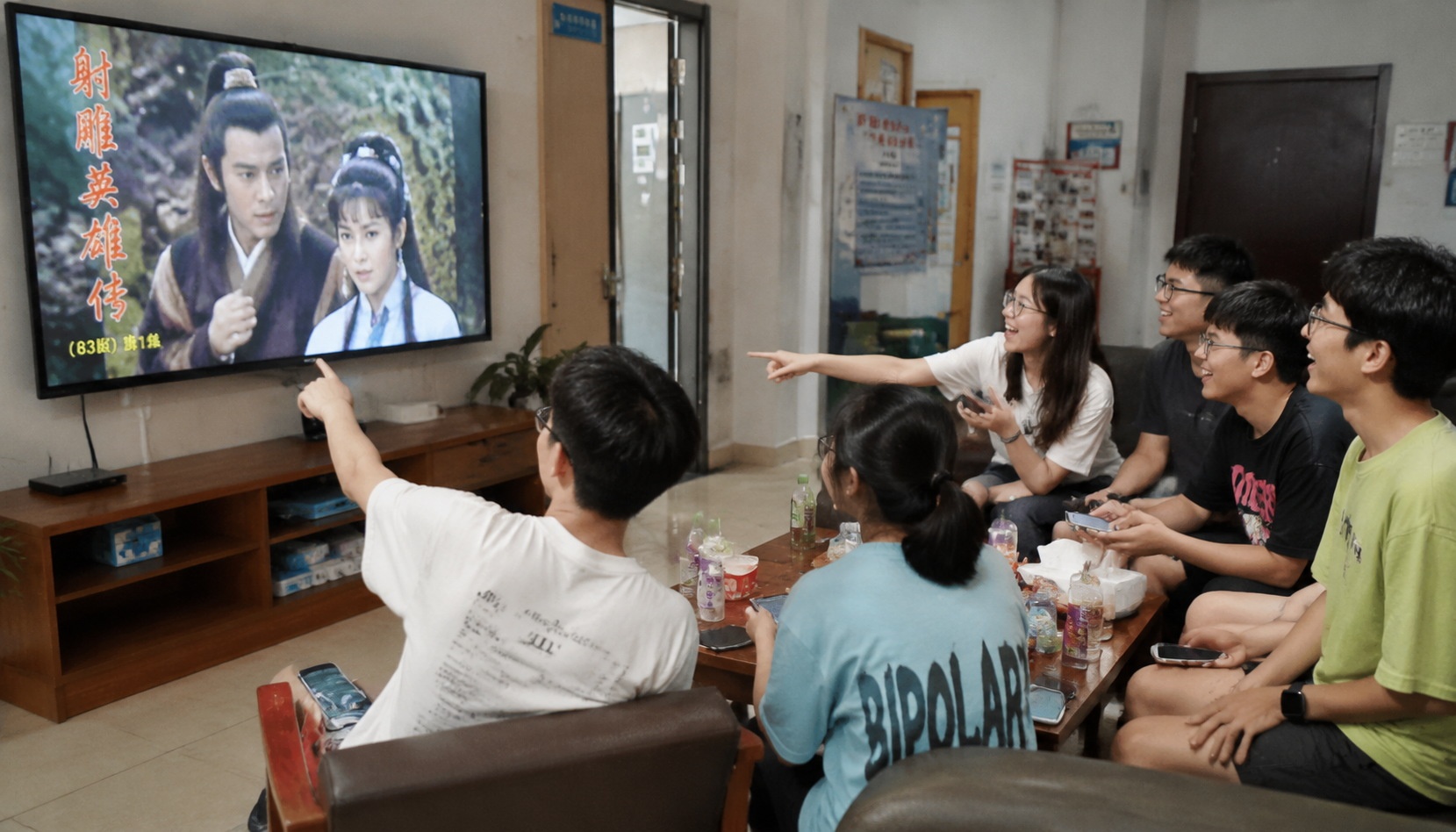 Chinese university students gathered around a TV watching the 1983 Legend of the Condor Heroes, laughing together.