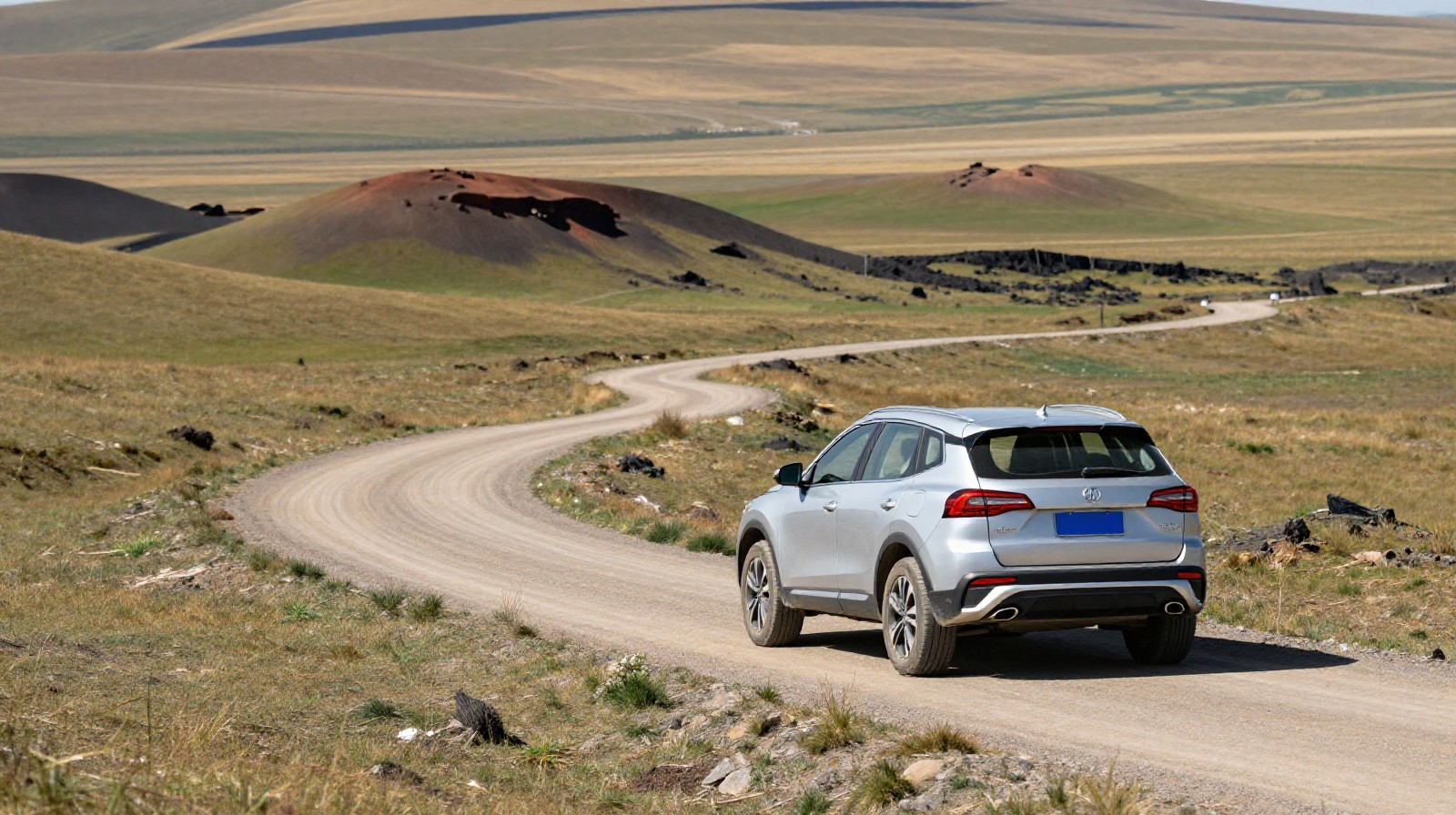 Silver SUV driving on a dirt road through grasslands and volcanic hills in Zhangjiakou