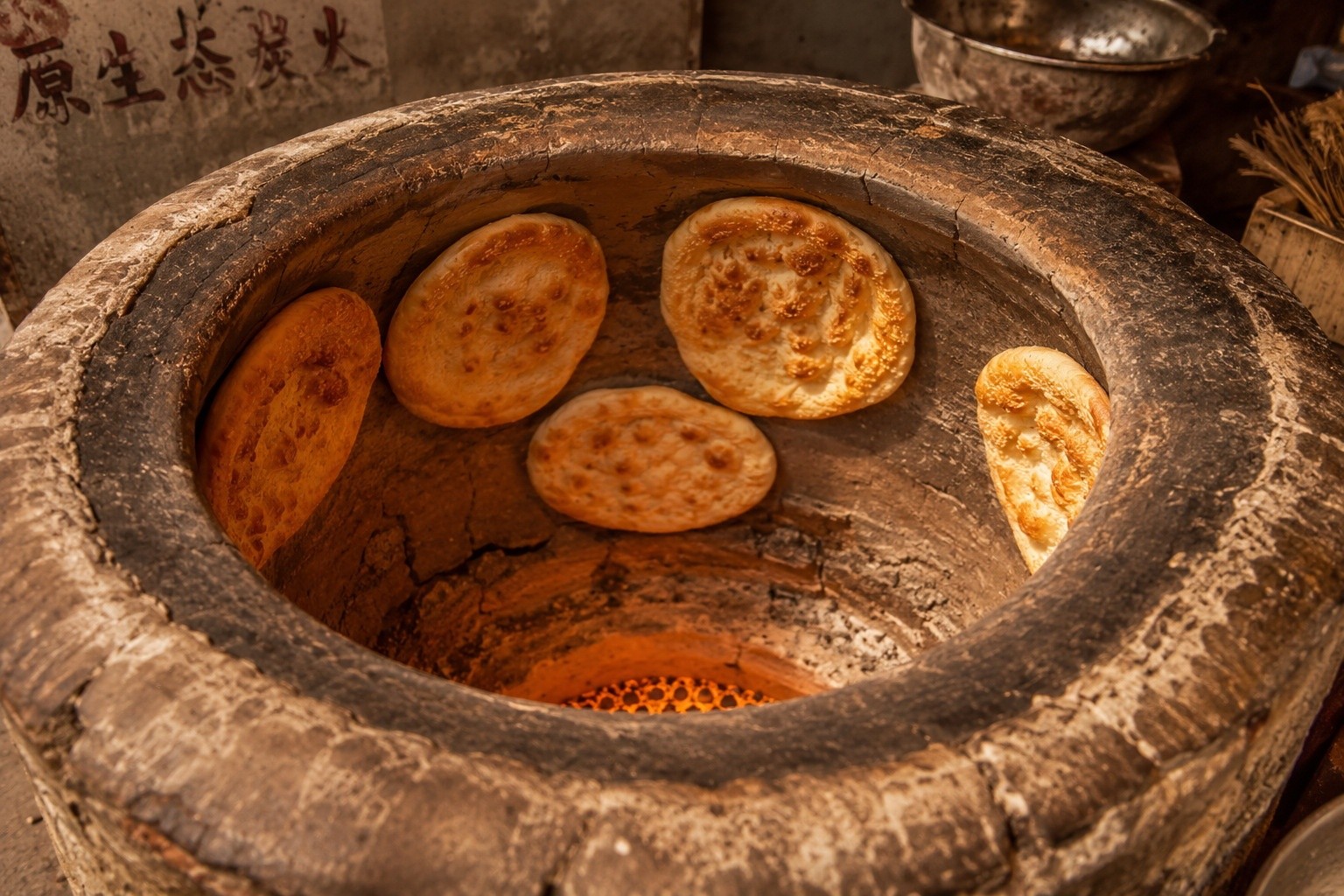 Traditional clay tandoor oven used for baking Roujamo flatbread in China, showing dough adhering to the hot walls.
