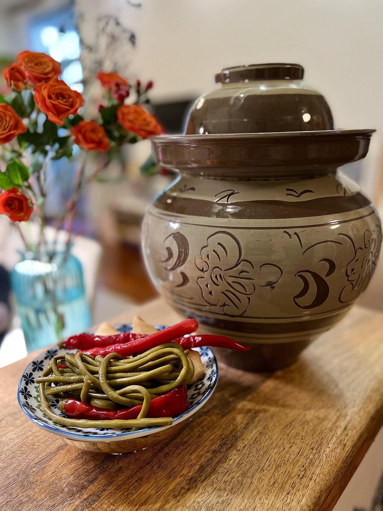 Sichuan mother's hands packing fresh vegetables into a clay pickle jar in a traditional home kitchen with natural light