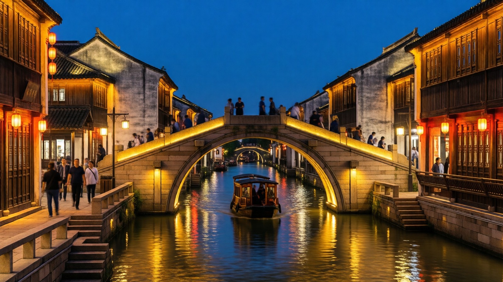 Illuminated historic stone bridge and pagodas on the Grand Canal in Hangzhou at night, with a tourist boat and pedestrians.