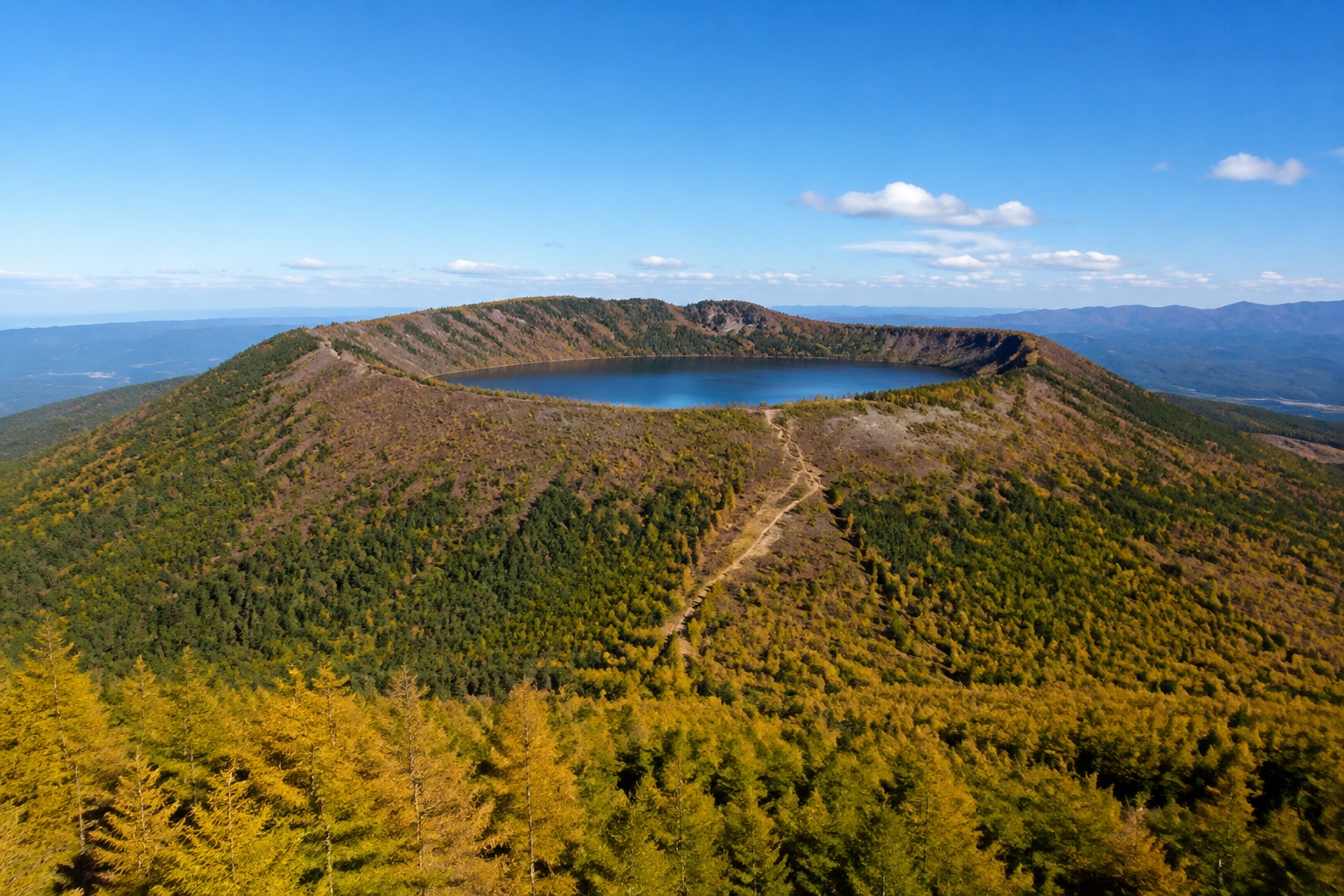 Panoramic view of Arxan Tianchi crater lake on a dormant volcano in autumn, with hikers on the trail below