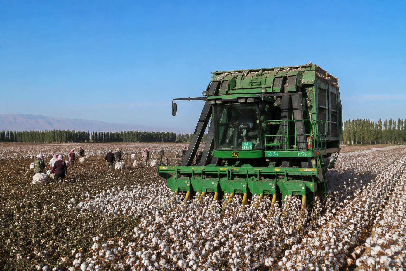 A John Deere cotton picker harvesting in a Xinjiang cotton field, with seasonal workers hand-picking cotton in the background, illustrating the coexistence of mechanized and manual labor.