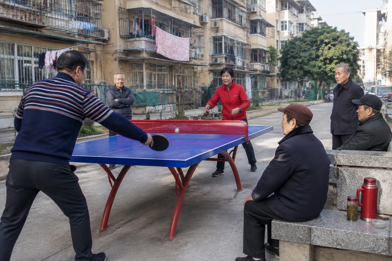 Retired residents watch a table tennis game at a concrete court between apartment buildings in Nanjing