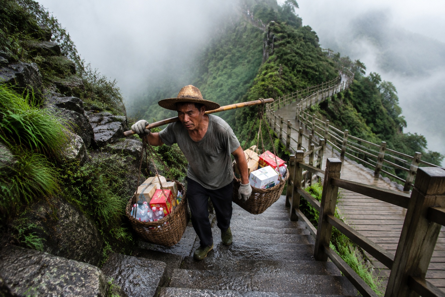 Carrier carrying heavy supplies on bamboo pole ascending Fanjingshan stone steps