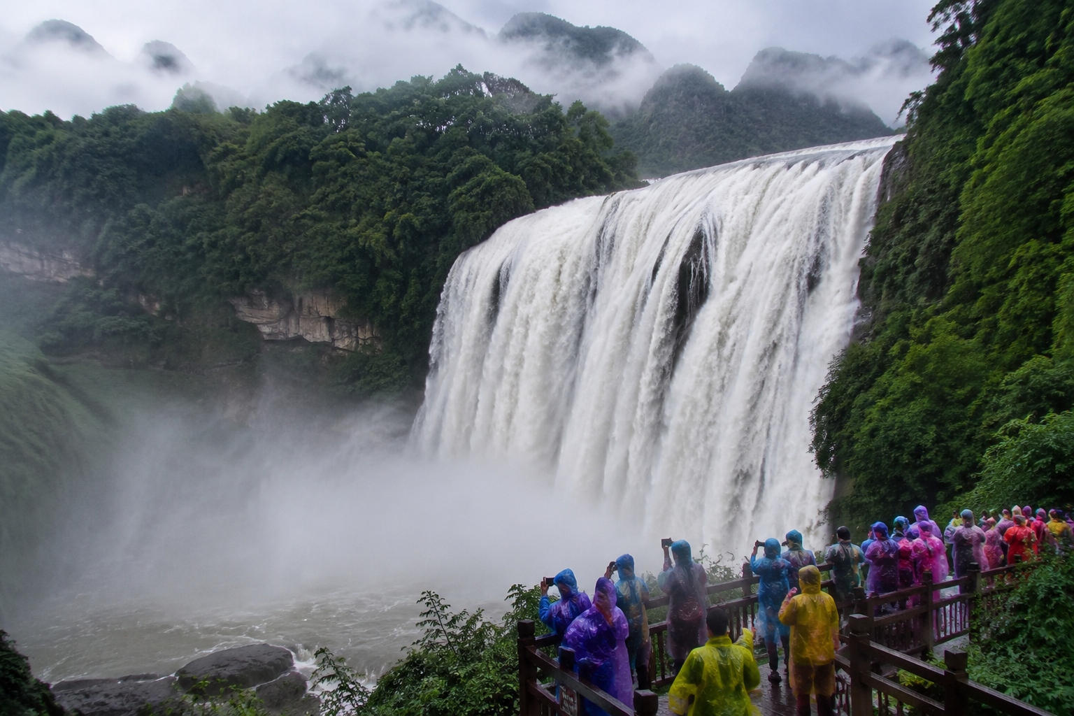 Huangguoshu Waterfall at peak flow during summer rainy season with tourists on a wet viewing platform