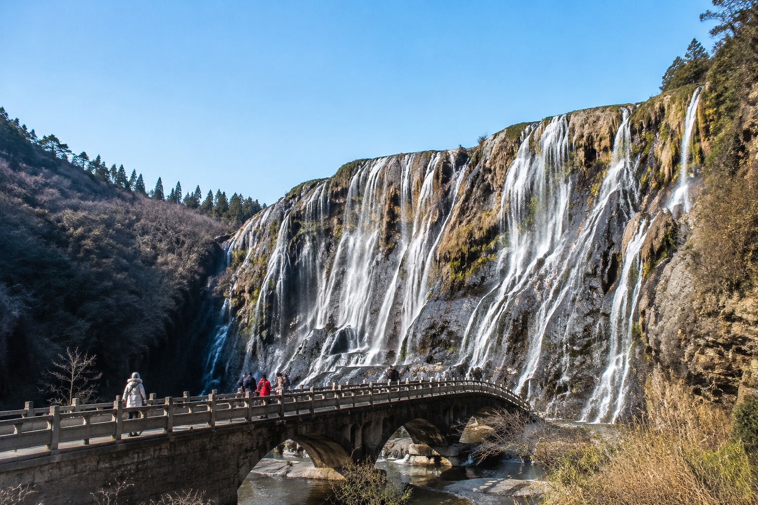 Huangguoshu Waterfall in winter with a gentle stream and sparse visitors on a stone bridge