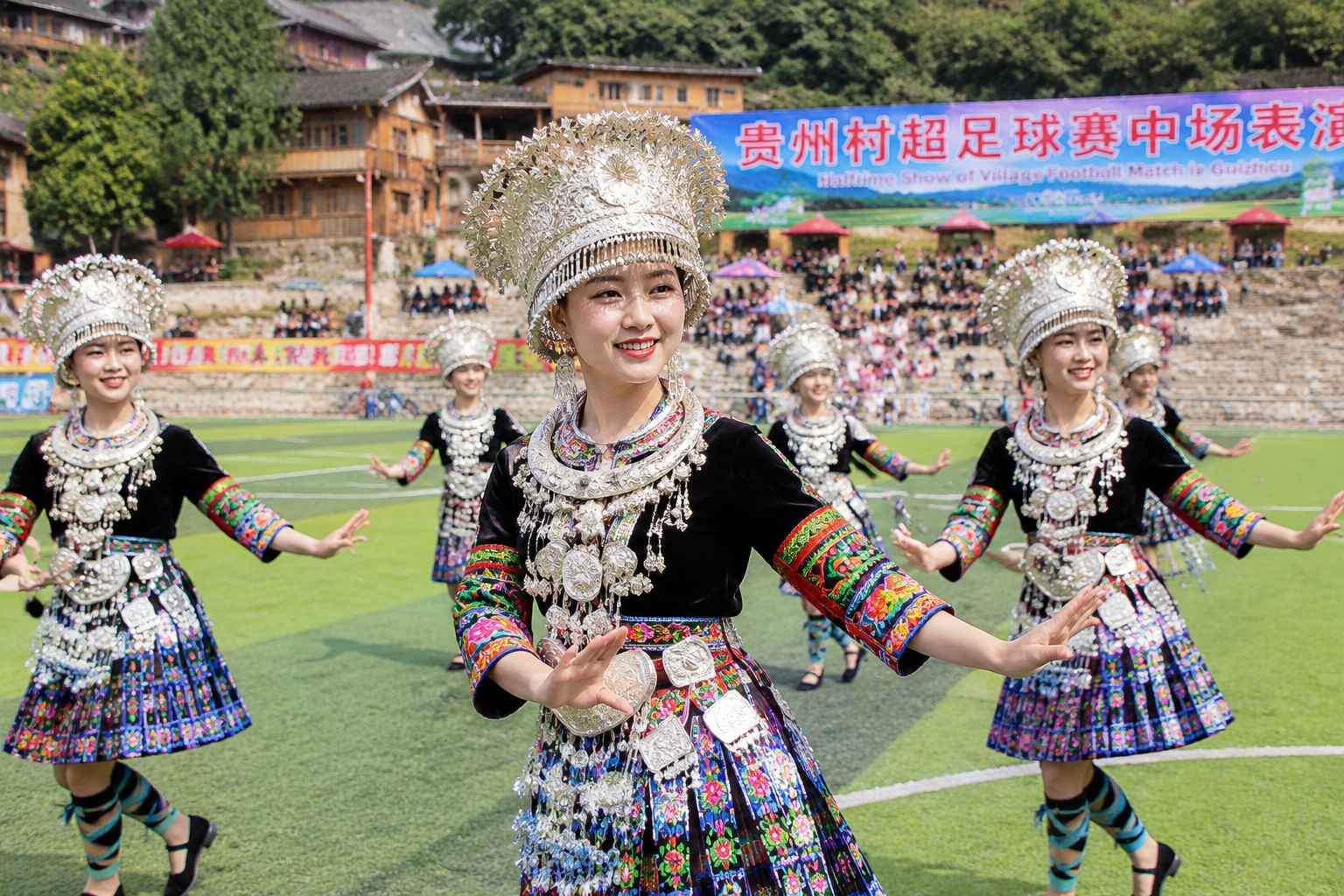 Dong women in traditional silver headpieces performing a folk song at halftime during a Village Super League match.
