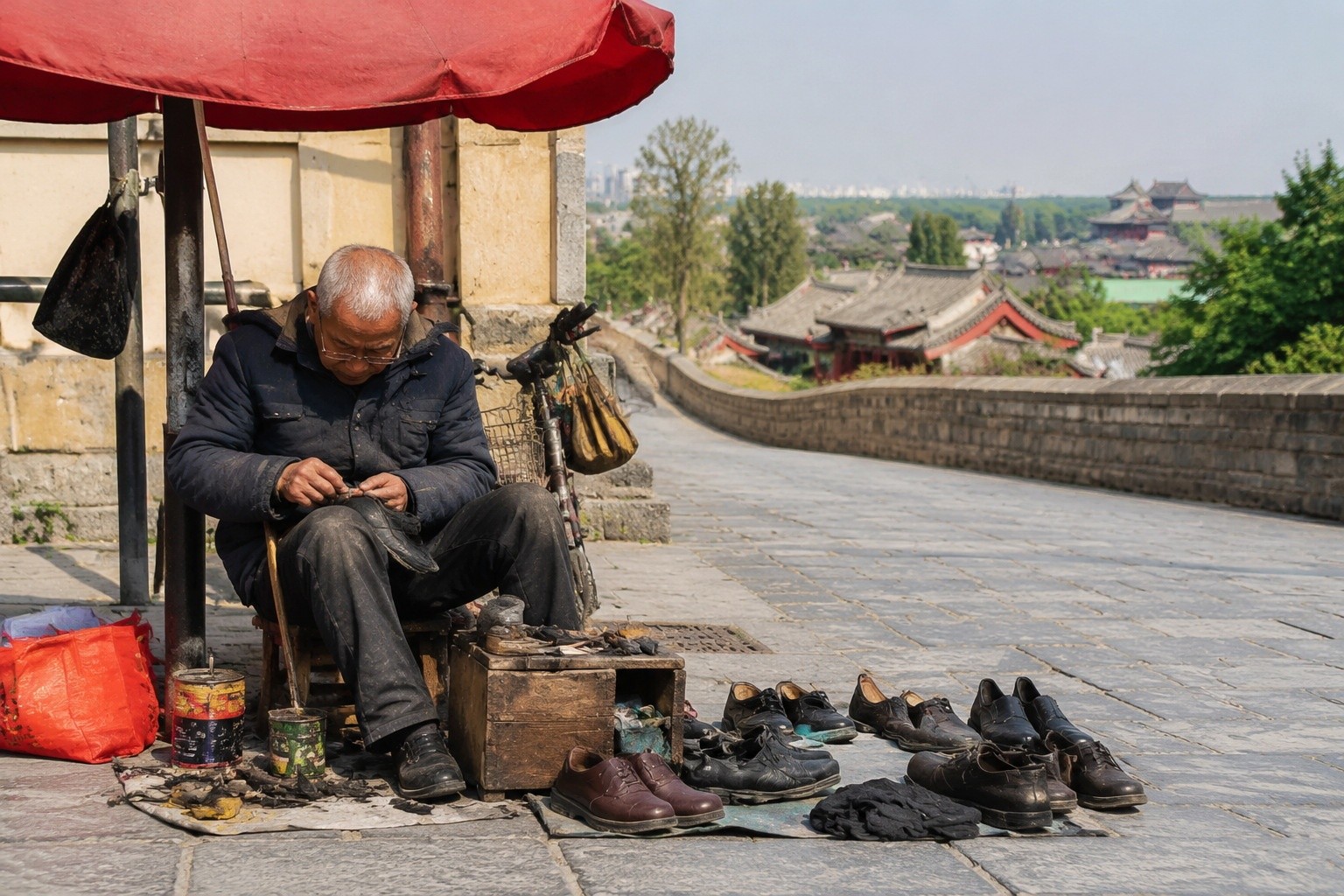 Elderly man repairing shoes on a sidewalk in Qufu, China, under a faded red umbrella, with tools and shoes around him, showing everyday street life.