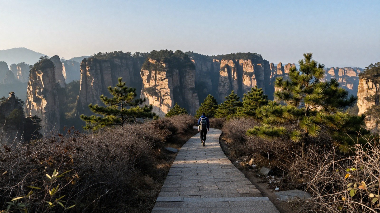 Hiking trail on Tianzi Mountain in Zhangjiajie with a lone hiker and distant misty pillars.