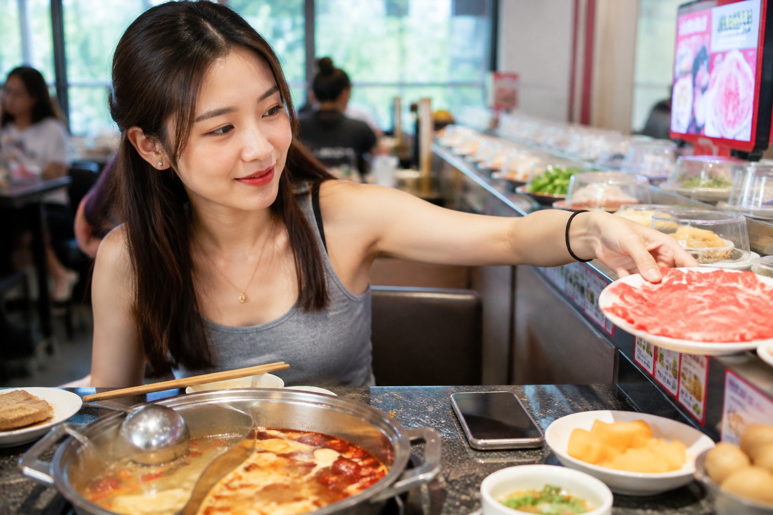Young Chinese woman picking a plate of sliced beef from a conveyor belt at a solo hot pot restaurant
