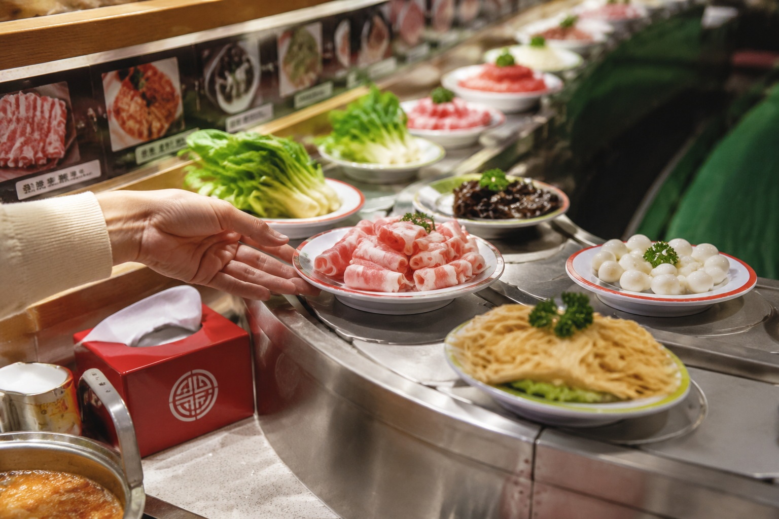 Small fresh ingredients on plates move along a conveyor belt in a Chinese rotating hot pot restaurant.