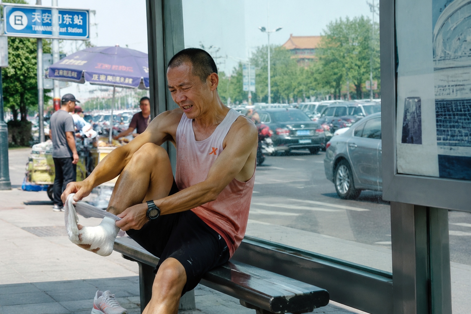 A tired runner sits on a bus stop bench in Beijing checking his blistered foot during a rest break on the ring road run