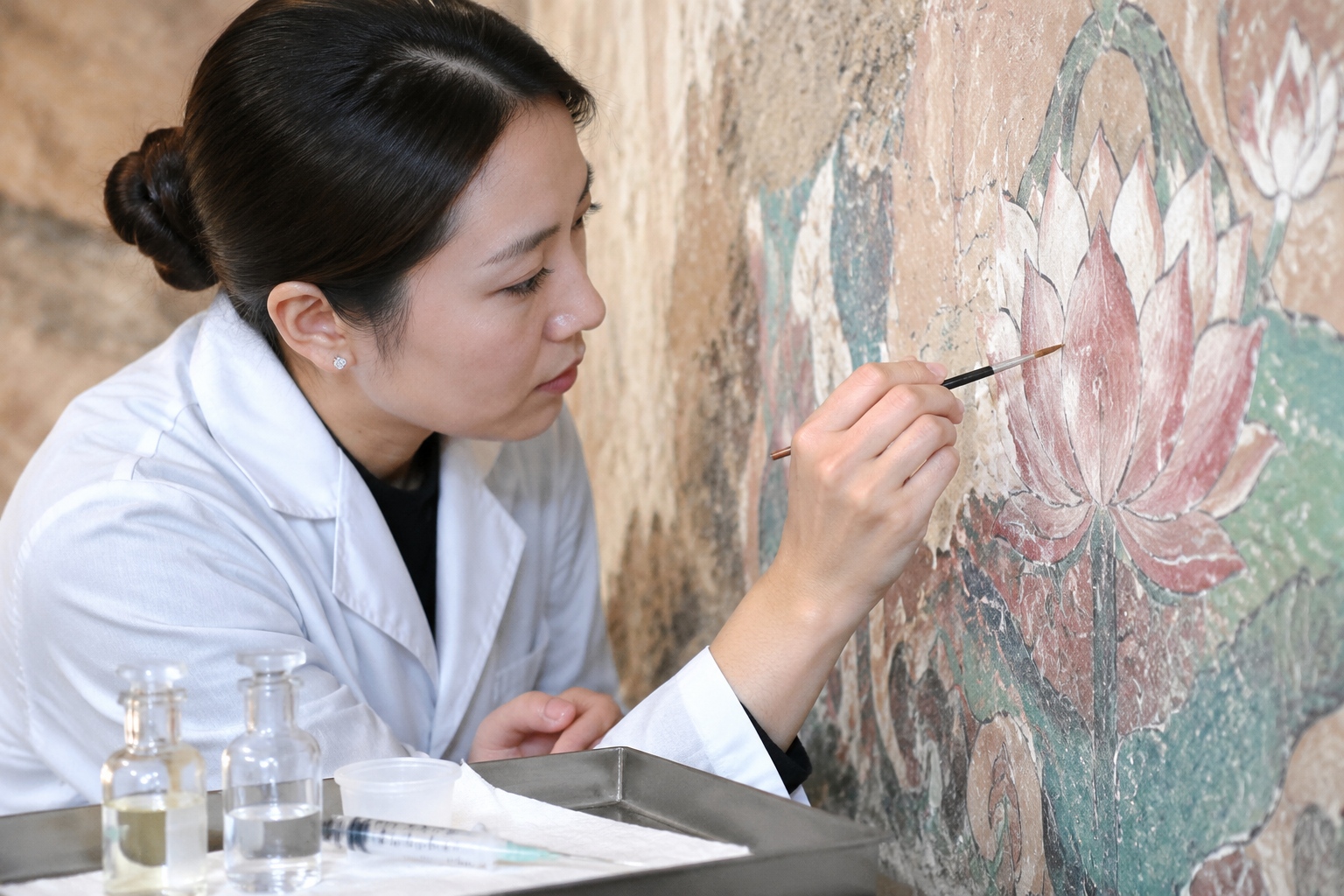 Female conservator restoring a Dunhuang mural with a fine brush and syringe in Cave 158