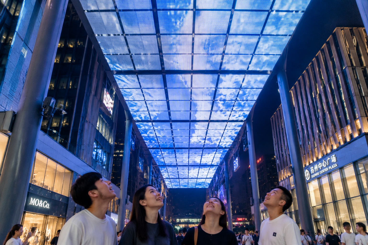 Looking up at the 80,000-screen LED canopy in Suzhou Industrial Park, showing the grid structure against the night sky with pedestrians below.