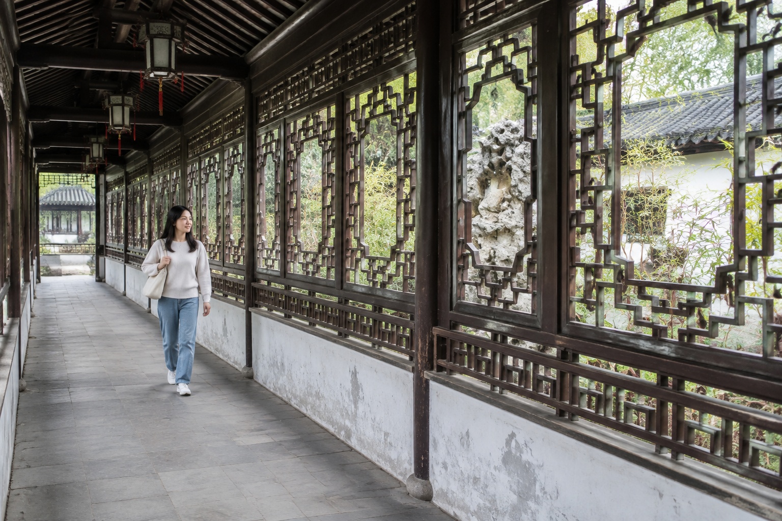 A row of carved lattice windows in different patterns along a corridor at Canglang Pavilion, each framing bamboo and rockery in Suzhou