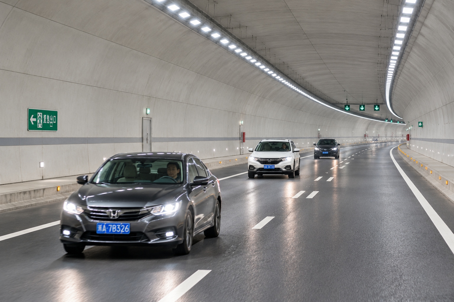 Cars driving through a newly opened road tunnel in China, lit by continuous strips of ceiling lights along the concrete lining